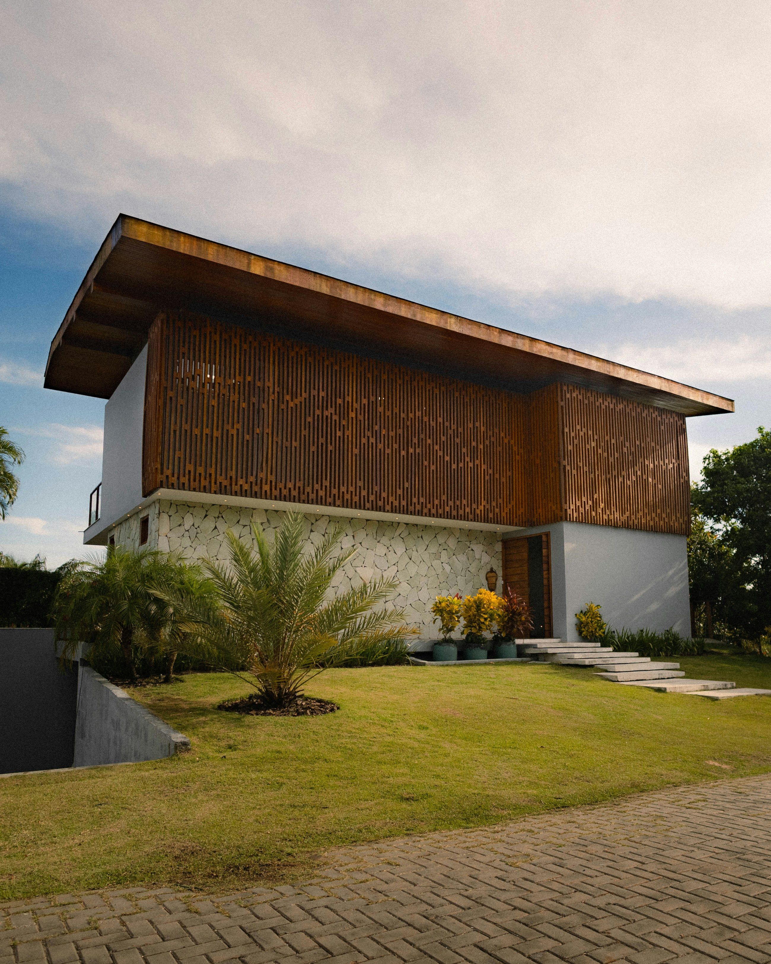 Casa de dois pavimentos com fachada em ripado de madeira, base em pedra natural e jardim tropical (imagem ilustrativa)